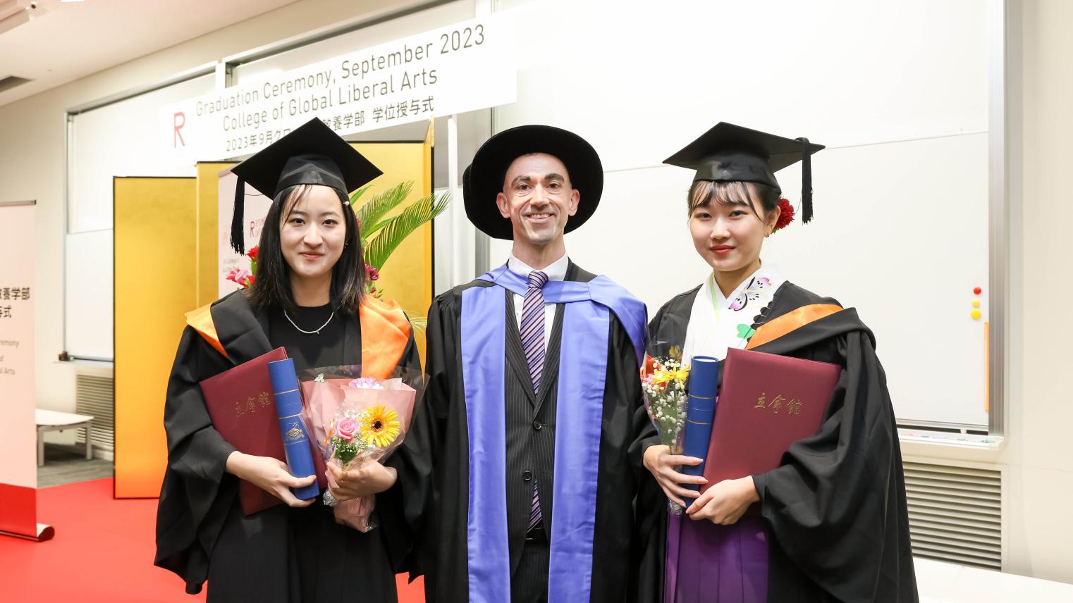 Ritsumeikan University - 1 Three people standing in graduation robes and hats