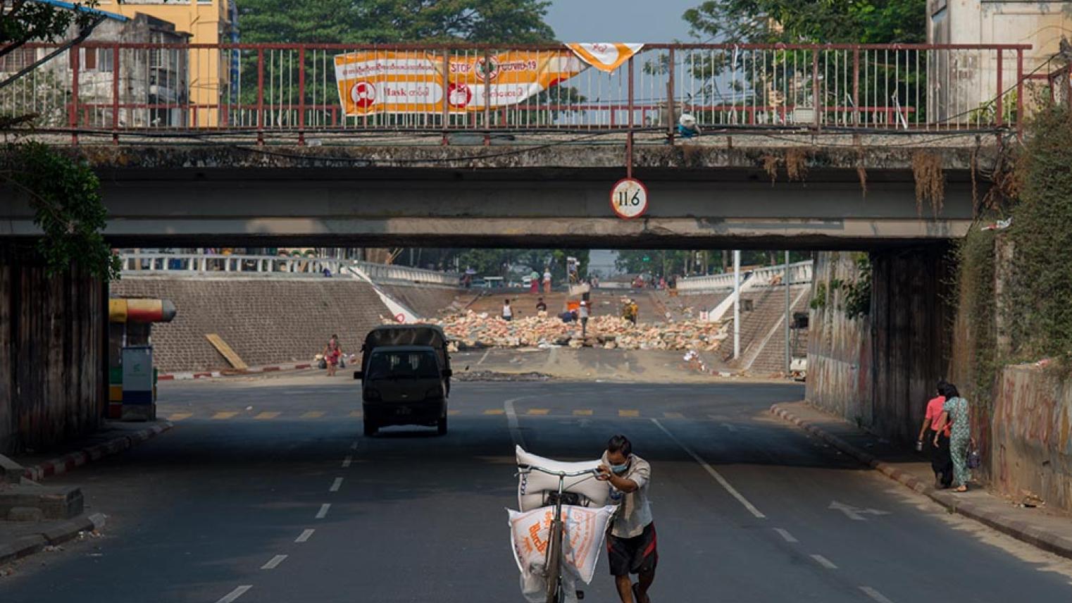 A man is pushing a bicycle, and a barricade at the intersection of Myanmar street.